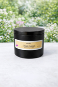 Black candle jar with 'Dream Garden' label on a white surface with a blurred natural background