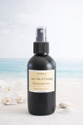 Black spray bottle labeled 'Sea Salt & Orchid' on a white background with blurred orchids.